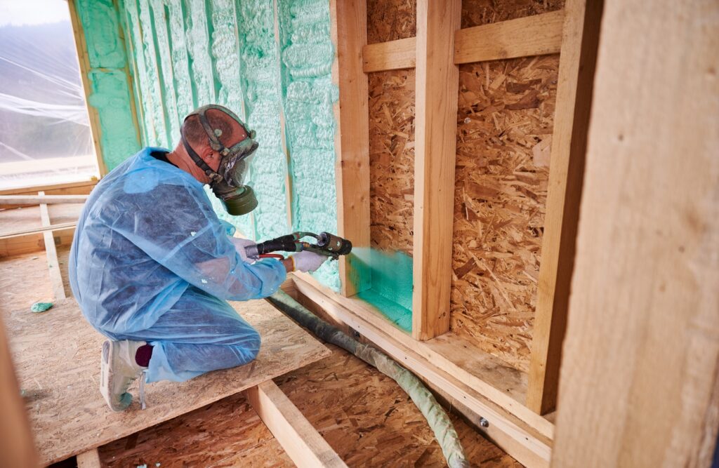 Worker spraying polyurethane foam for insulating wooden frame house.